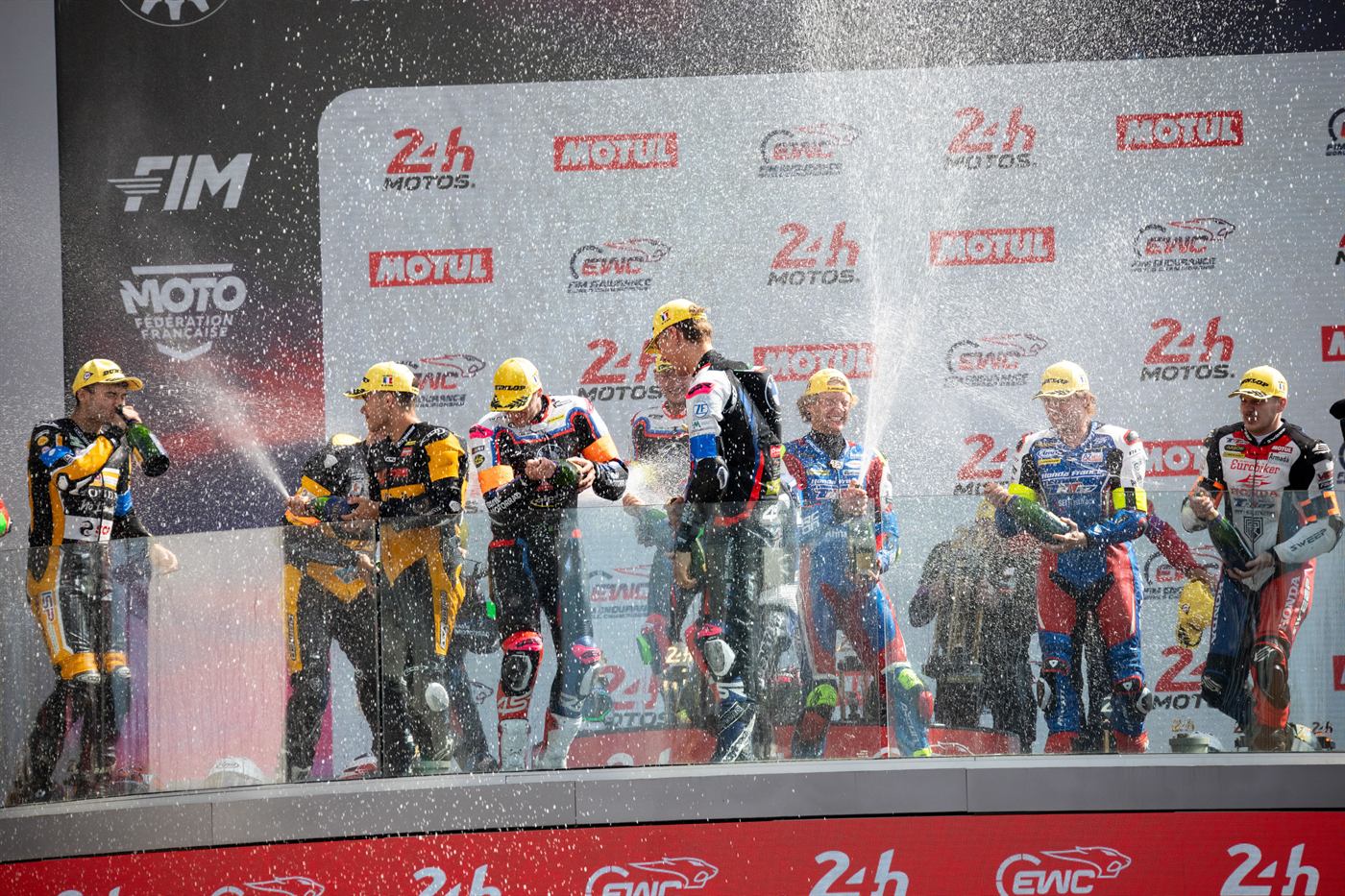 Arrivée des 24 Heures Motos 2026 : les pilotes vainqueurs fêtent la victoire au champagne devant les logos 24H Motos et EWC FIM Endurance