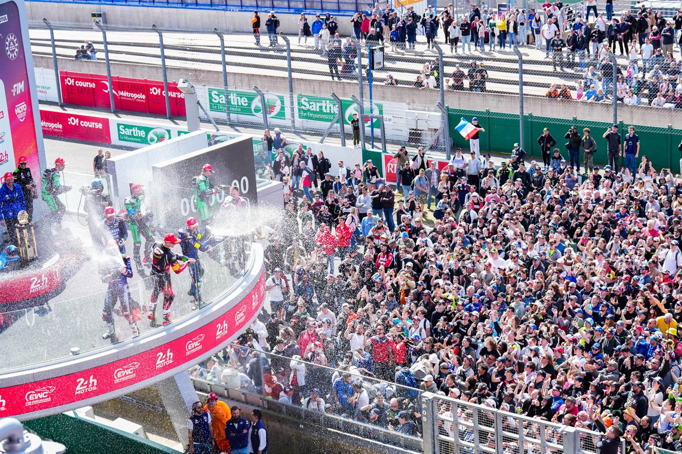 Podium des 24 Heures Motos 2026 : le YART Yamaha Official EWC Team fête sa victoire au champagne devant une foule dense au Mans